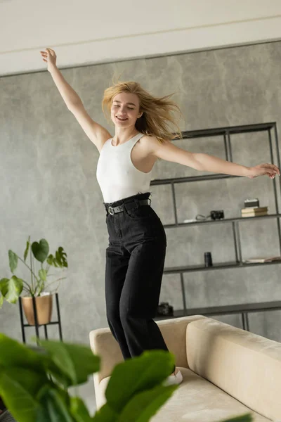 Excited woman with closed eyes and outstretched hands dancing on sofa at home — Stock Photo