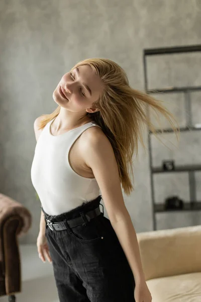 Pretty blonde woman in white tank top dancing with closed eyes at home — Stock Photo