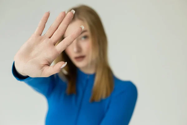 Blurred blonde woman showing stop sign with outstretched hand isolated on grey — Stock Photo