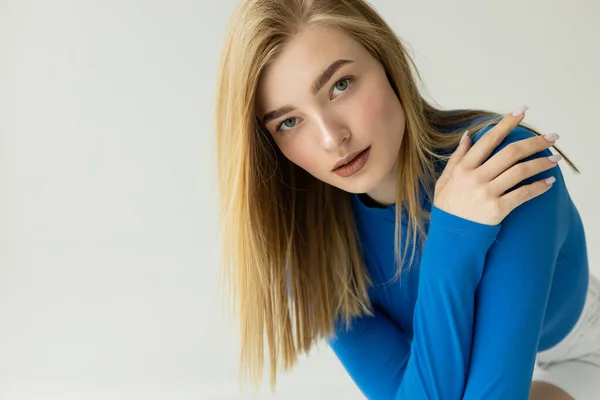 Blonde woman with natural makeup wearing blue turtleneck and looking at camera isolated on grey — Stock Photo