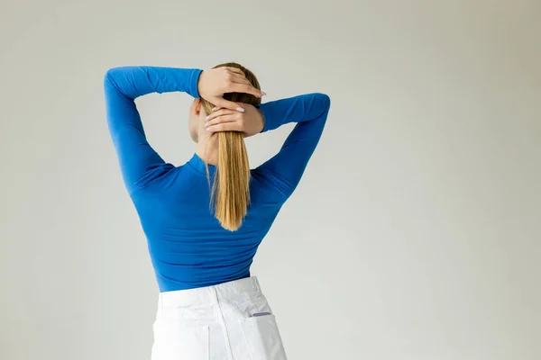 Back view of woman in blue turtleneck and white shorts fixing hair isolated on grey — Stock Photo