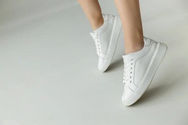 Cropped view of woman in white leather sneakers standing on tiptoes on grey background — Stock Photo