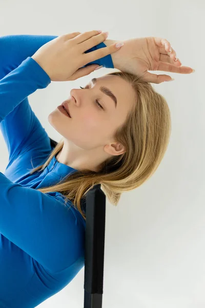 Young and sensual woman with closed eyes and natural makeup posing with hands above head isolated on grey — Stock Photo