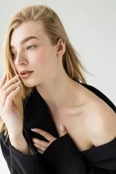 Portrait of young blonde woman with naked shoulder posing with hand near face isolated on grey — Stock Photo