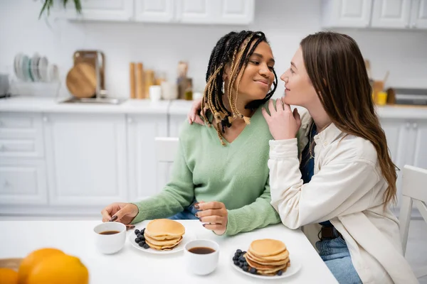 Веселая лесбиянка обнимает африканскую американскую подружку во время завтрака — стоковое фото