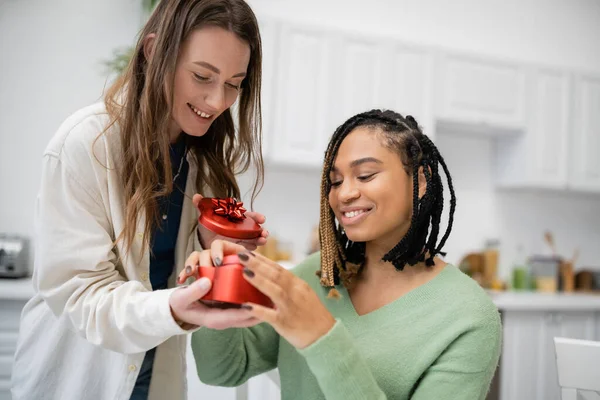 Glückliche lesbische Frau in herzförmiger Geschenkbox neben lächelnder afrikanisch-amerikanischer Freundin — Stockfoto