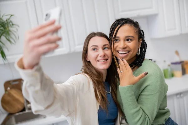 Mulher lésbica tomando selfie enquanto feliz afro-americana namorada mostrando anel de noivado no dedo — Fotografia de Stock