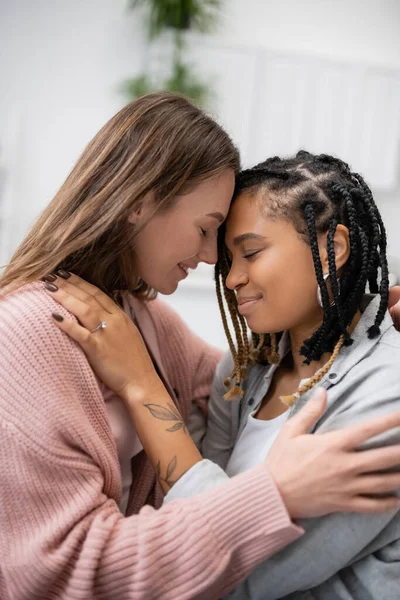 Mujer lesbiana afroamericana tatuada con anillo de compromiso abrazando a su novia sonriente - foto de stock