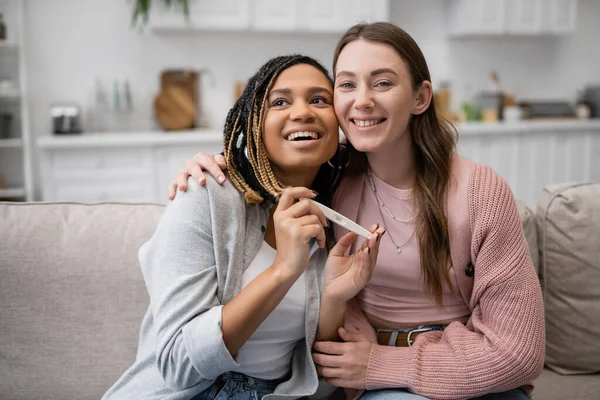 Feliz Africano americano e lésbico mulher segurando teste de gravidez perto alegre namorada — Fotografia de Stock