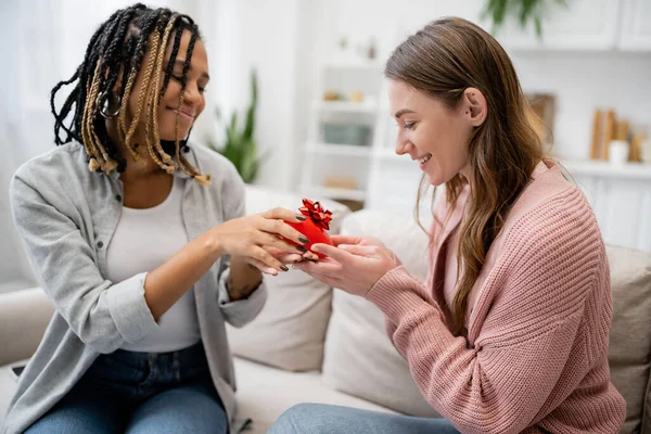 Glückliche afrikanisch-amerikanische und lesbische Frau schenkt ihrer freudigen Freundin ein herzförmiges Geschenk — Stockfoto