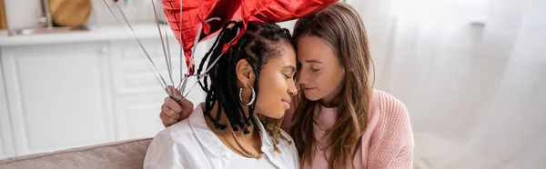 Femme lesbienne sensuelle tenant des ballons rouges près de petite amie afro-américaine le jour de la Saint-Valentin, bannière — Photo de stock
