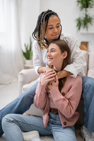 Smiling african american lesbian woman with dreadlocks hugging girlfriend in living room — Stock Photo