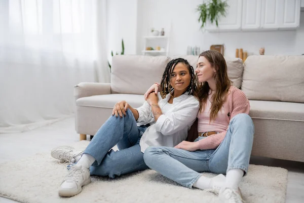 Glückliche lesbische Frau sitzt mit tätowierter afrikanisch-amerikanischer Freundin in der Nähe von Couch — Stockfoto