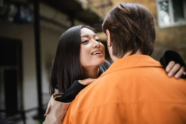 Smiling asian woman hugging boyfriend in outdoor cafe — Stock Photo