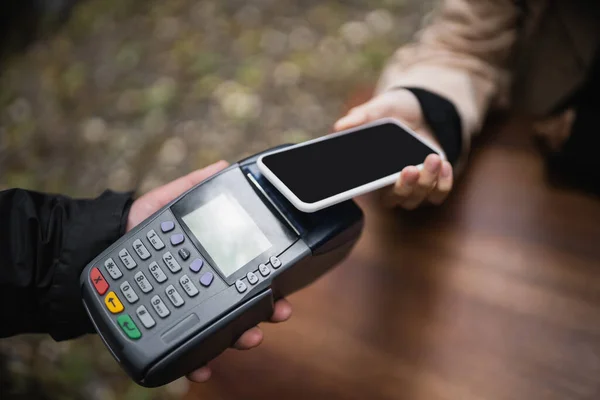 Cropped view of waiter holding payment terminal near customer with smartphone in outdoor cafe — Stock Photo