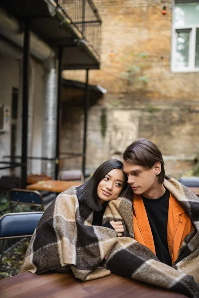 Young asian woman in blanket hugging boyfriend on terrace of cafe — Stock Photo