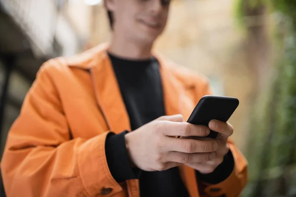 Cropped view of blurred man in jacket using smartphone outdoors — Stock Photo