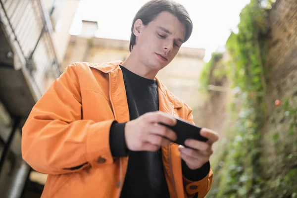 Low angle view of young man using cellphone on terrace of cafe — Stock Photo