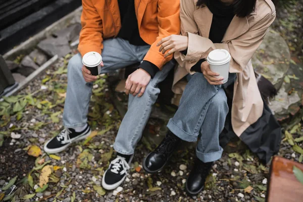 Cropped view of stylish young couple holding paper cups on terrace of cafe — Stock Photo