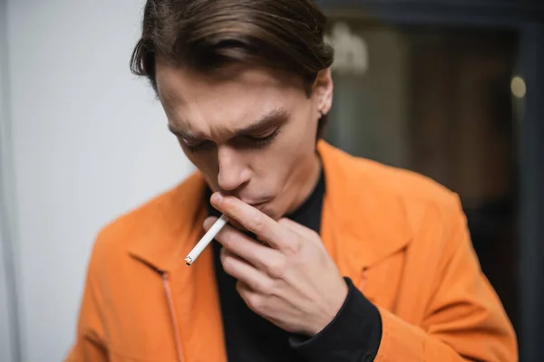 Young man in jacket smoking cigarette outdoors — Stock Photo