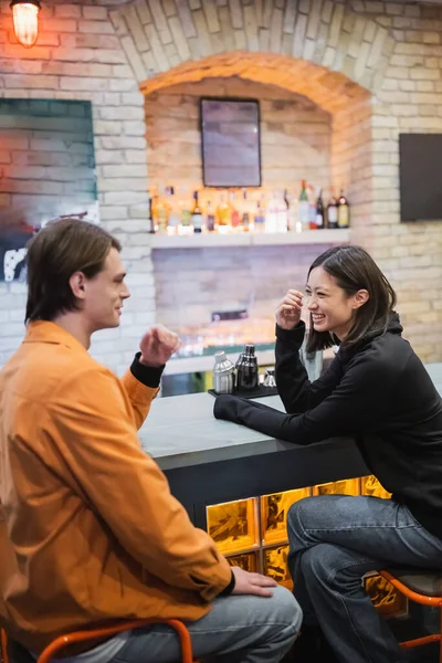 Allegro interrazziale coppia ridere e parlare vicino bar in caffè — Foto stock