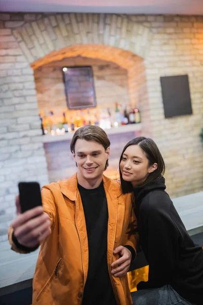 Smiling multiethnic couple taking selfie on cellphone in cafe — Stock Photo