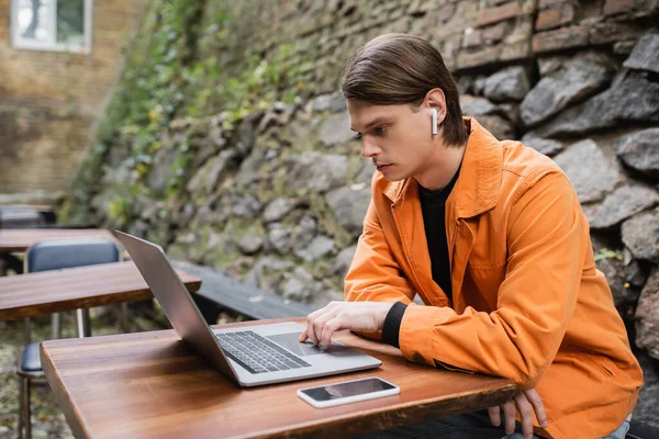 Uomo alla moda in auricolare utilizzando il computer portatile sulla terrazza del caffè — Foto stock