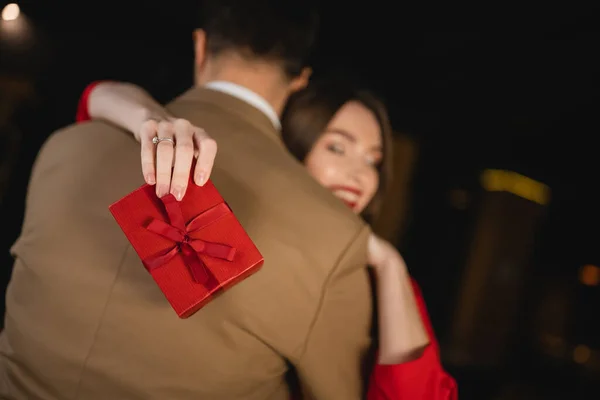 Blurred and cheerful woman holding present and hugging boyfriend on valentines day — Stock Photo