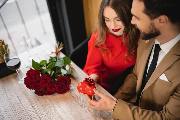 Hochwinkelaufnahme eines bärtigen Mannes, der einer glücklichen Freundin am Valentinstag ein herzförmiges Geschenk mit Verbeugung überreicht — Stockfoto