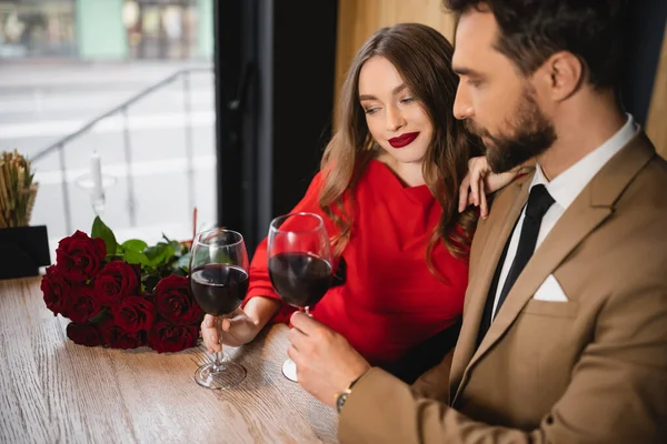 Bearded man clinking glasses of red wine with happy girlfriend on valentines day — Stock Photo