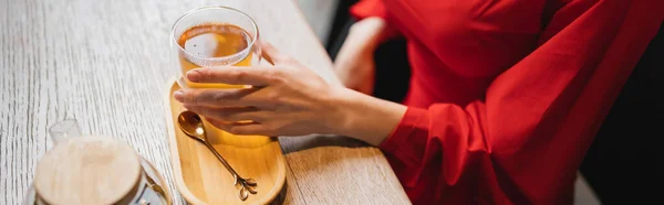 Vue recadrée de la femme en robe rouge tenant tasse en verre avec thé vert, bannière — Photo de stock