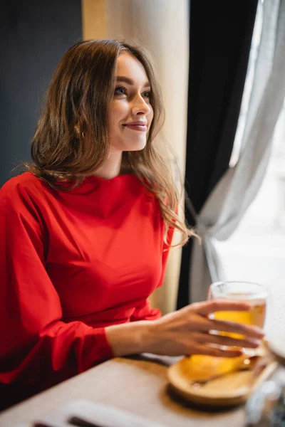 Mujer alegre sosteniendo taza de vidrio con té verde y mirando hacia otro lado - foto de stock