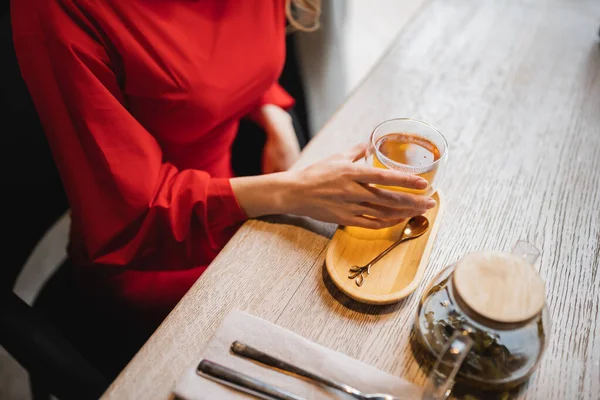 Vue recadrée de la femme en robe rouge tenant tasse en verre avec thé vert — Photo de stock