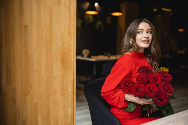 Alegre joven mujer sosteniendo ramo de rosas rojas y sonriendo en día de San Valentín - foto de stock