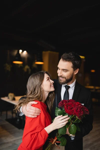 Весёлый мужчина обнимает счастливую девушку с букетом красных роз на День Святого Валентина — стоковое фото