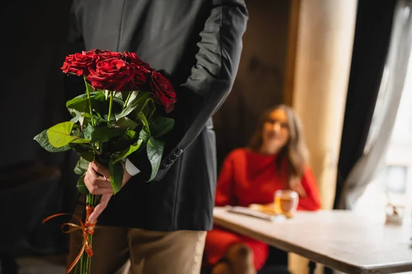Vista recortada del hombre escondiendo ramo de rosas rojas detrás de la espalda en el día de San Valentín - foto de stock