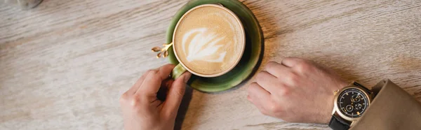 Top view of cropped man holding cup of cappuccino with latte art, banner — Stock Photo