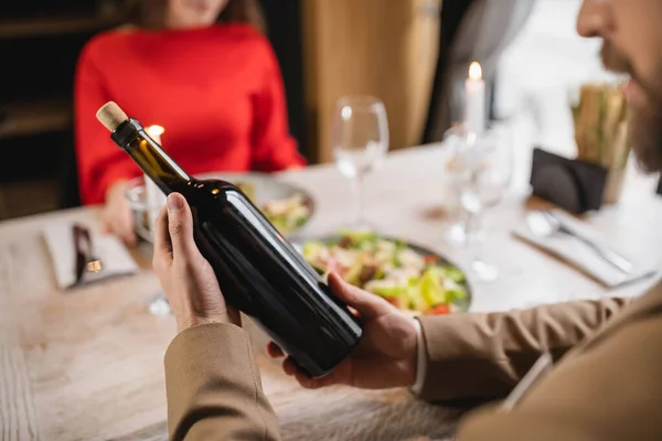 Cropped view of man holding bottle with wine near girlfriend during festive dinner on valentines day — Stock Photo