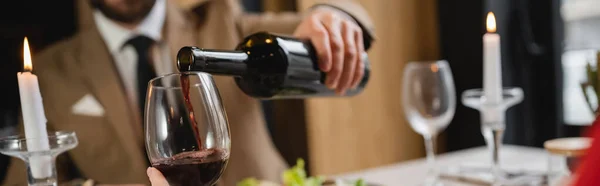 Cropped view of blurred man pouring red wine in glass of girlfriend during dinner on valentines day, banner — Stock Photo