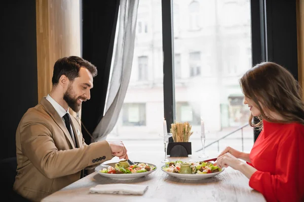 Side view of cheerful couple eating salad in restaurant on valentines day — Stock Photo