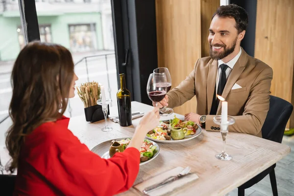 Alegre hombre y mujer tintineo vasos de vino tinto durante la cena en el día de San Valentín - foto de stock
