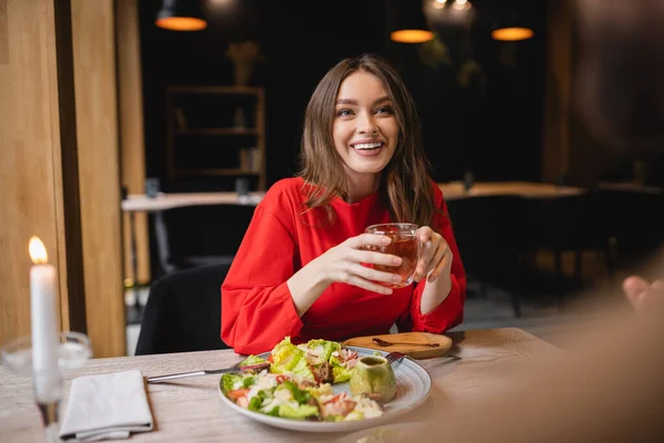 Mulher sorrindo segurando copo de vidro de chá verde e olhando para o homem borrado no restaurante — Fotografia de Stock