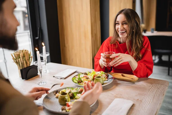 Smiling woman holding glass cup of green tea and talking with blurred man in restaurant — Stock Photo