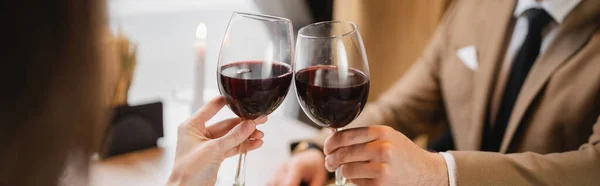 Cropped view of couple clinking glasses with red wine during celebration on valentines day, banner — Stock Photo