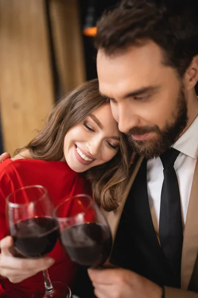Happy woman and bearded man clinking glasses with red wine during celebration on valentines day — Stock Photo