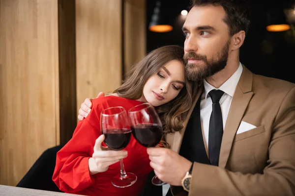 Молодая женщина и бородатый мужчина звонят бокалы с красным вином во время празднования Дня Святого Валентина — стоковое фото