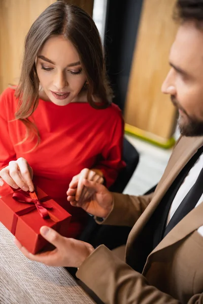 Bearded man in formal wear holding present near young woman in red dress on valentines day — Stock Photo