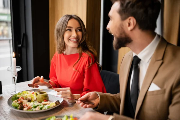 Pareja alegre en traje festivo mirándose en el restaurante durante la celebración en el día de San Valentín - foto de stock