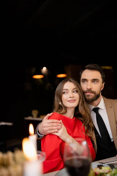 Hombre barbudo abrazando a mujer joven en vestido rojo en el día de San Valentín - foto de stock