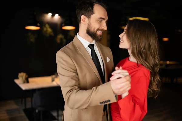 Seitenansicht eines glücklichen Mannes und einer glücklichen Frau in festlicher Kleidung, die sich Händchen haltend am Valentinstag anschauen — Stockfoto